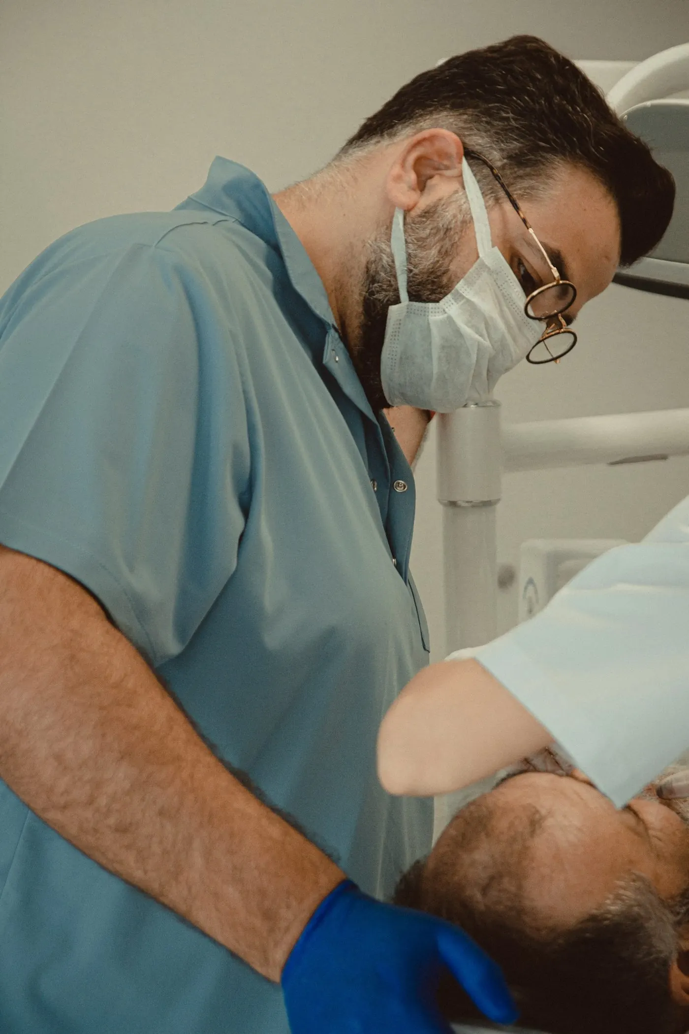 A dentist in scrubs and a mask treating a patient